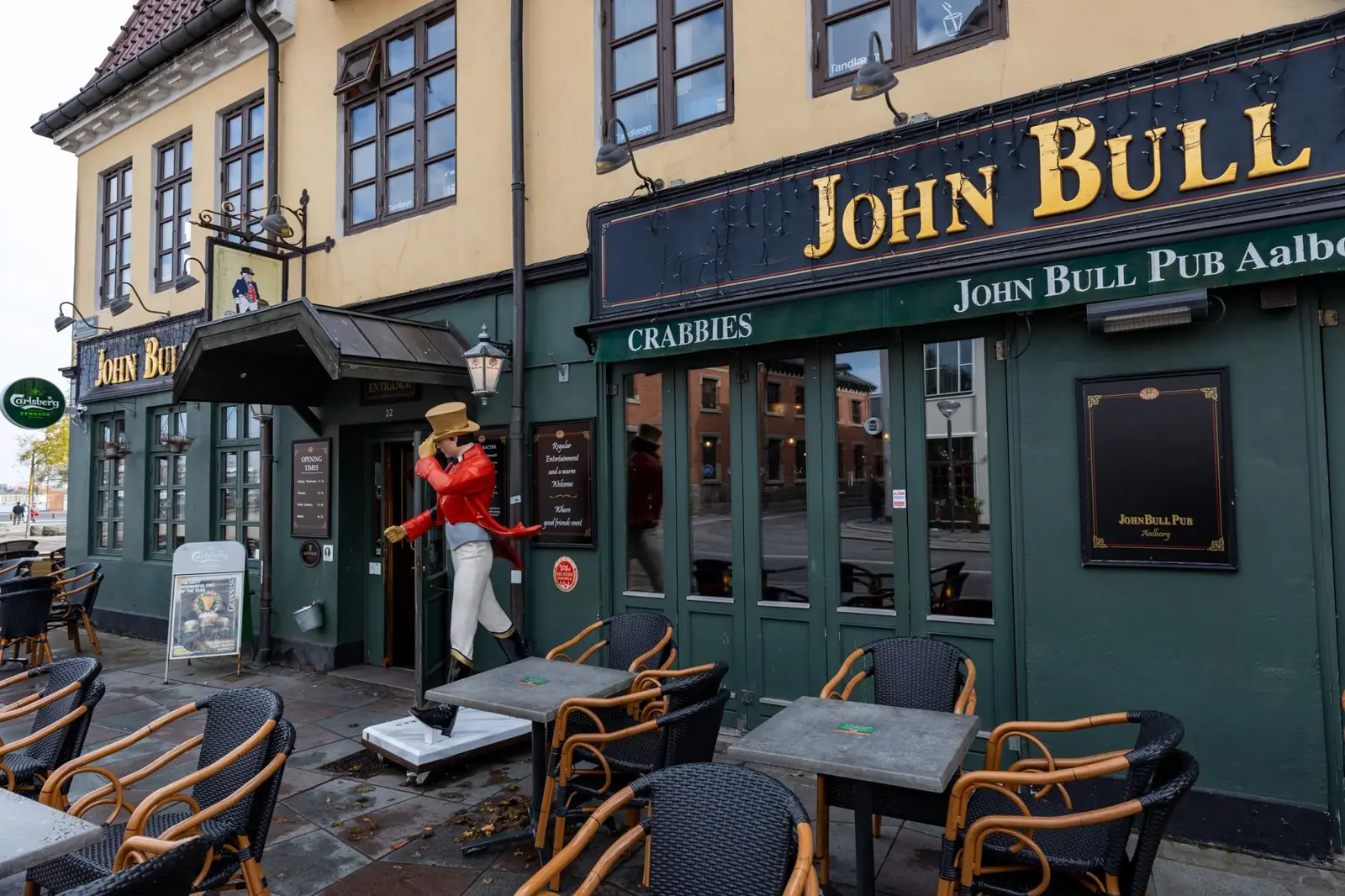 Exterior view of John Bull Pub in Aalborg with outdoor seating on a clear day.