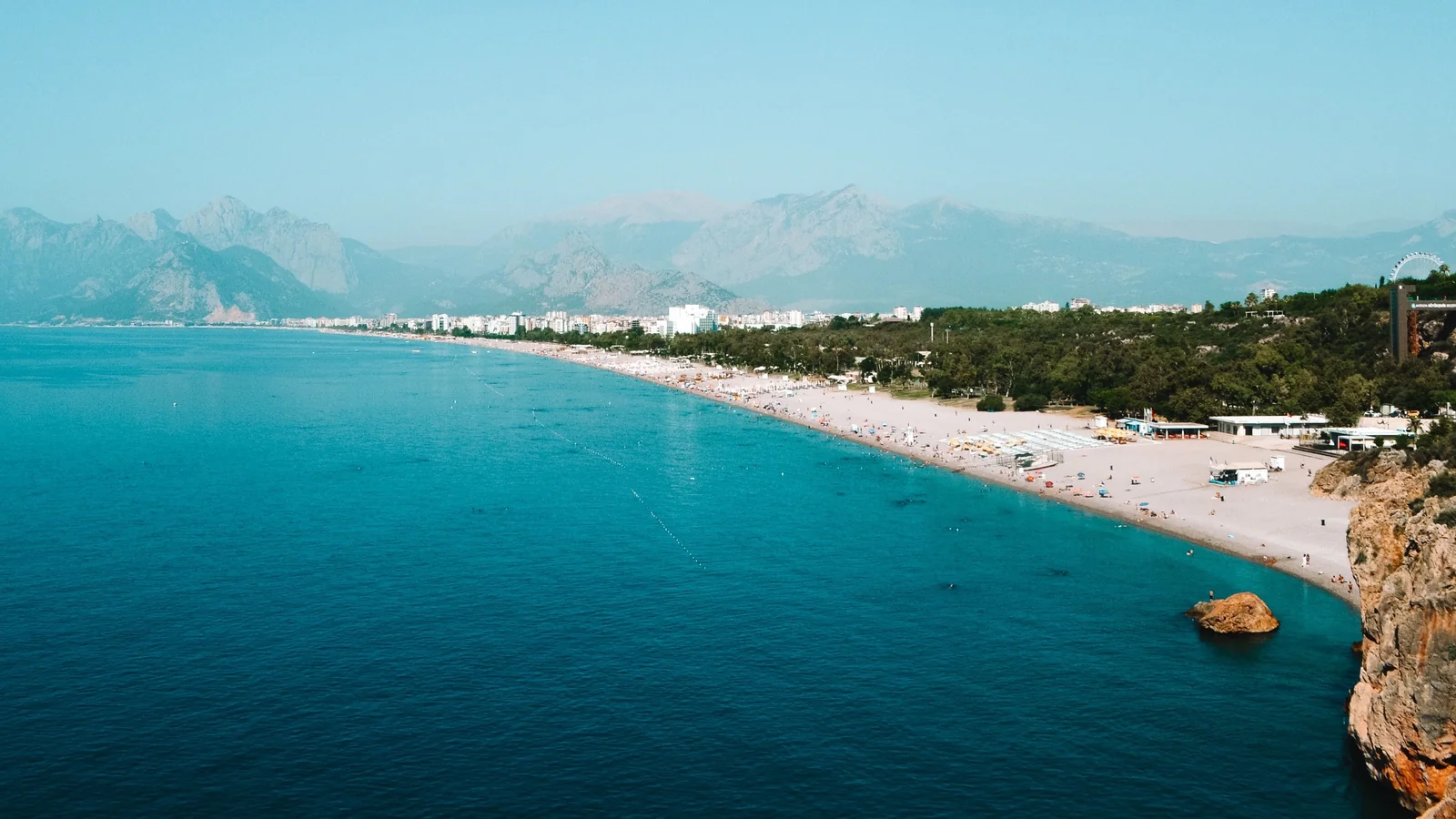 Konyaaltı Beach curving along Antalya’s western shore, with turquoise water and distant mountain silhouettes.