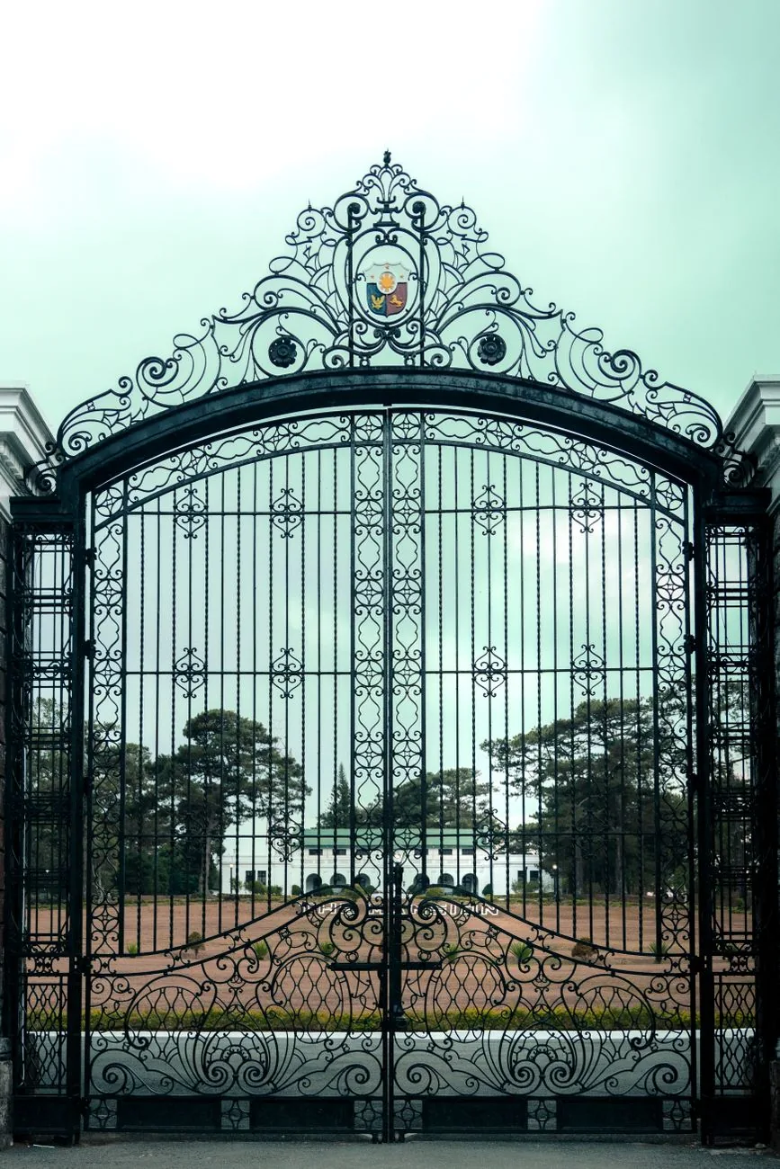 Ornate iron entrance gates of Baguio Mansion House with the white arched building and green roof beyond
