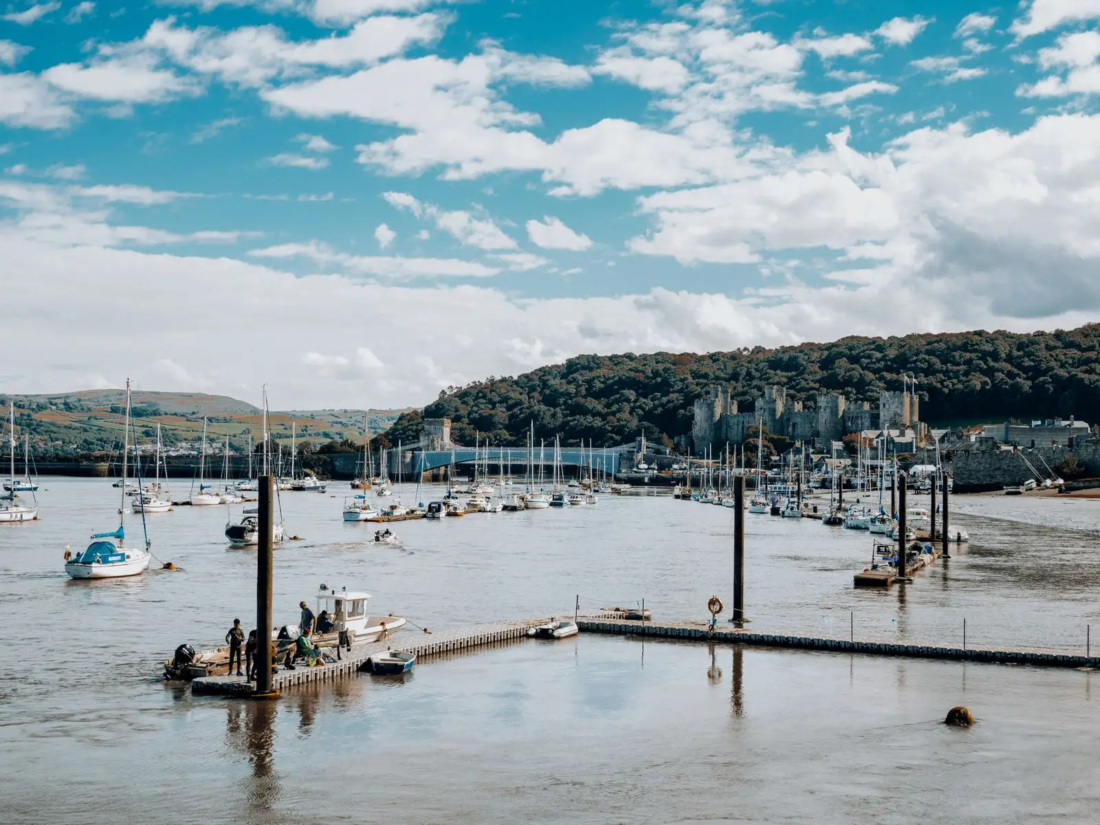 Boats moored in Conwy harbour with the estuary and wooded slopes beyond