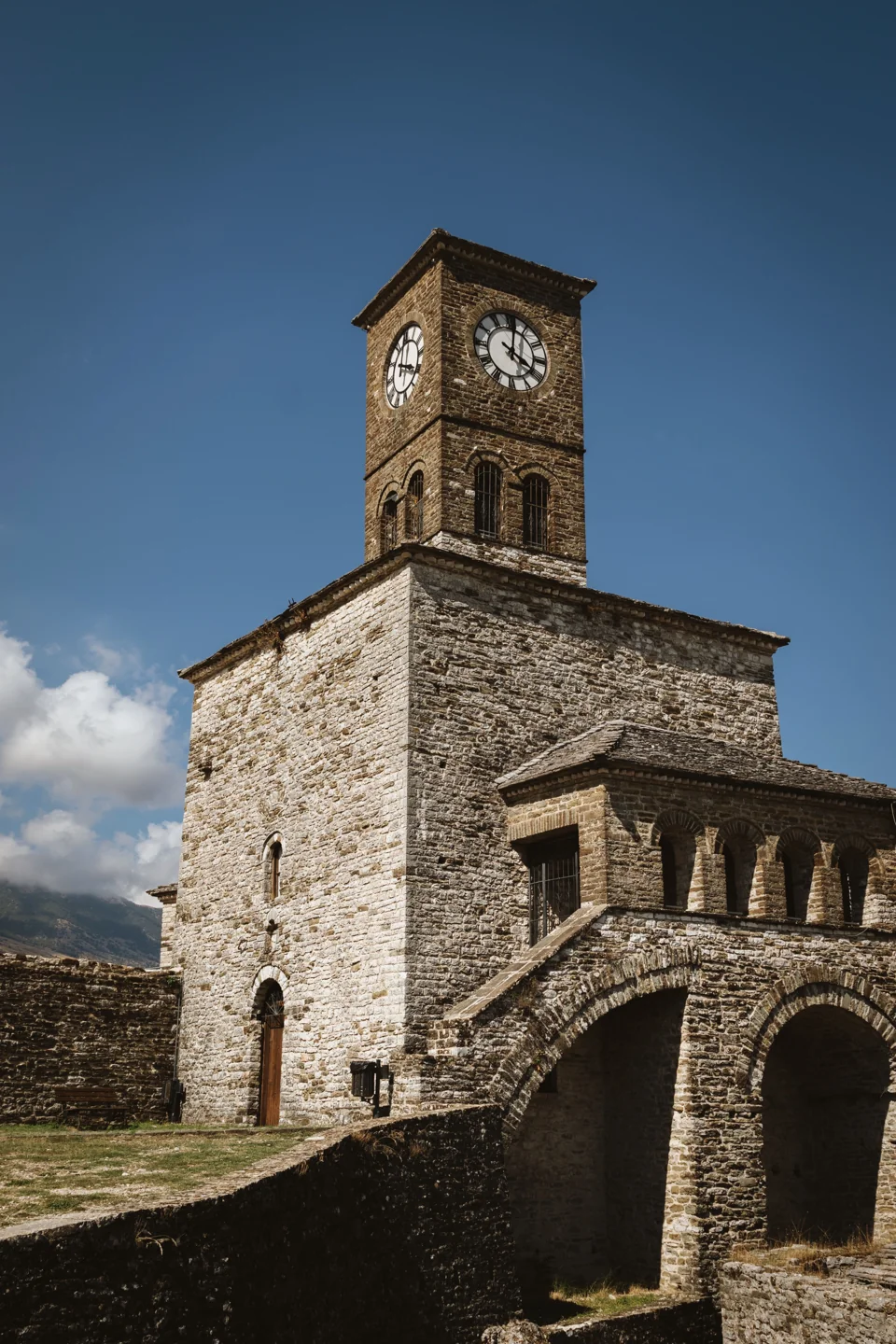 Gjirokastër Castle clock tower above its stone arcade beneath a blue sky