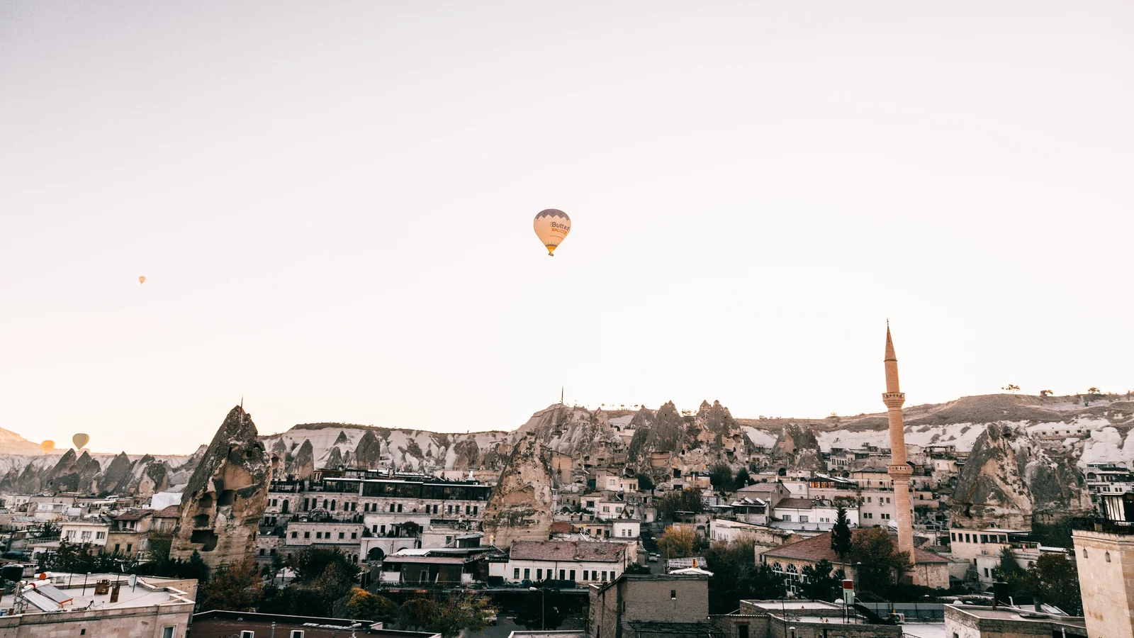 A hot-air balloon above Göreme’s stone buildings, minaret and surrounding rock formations.