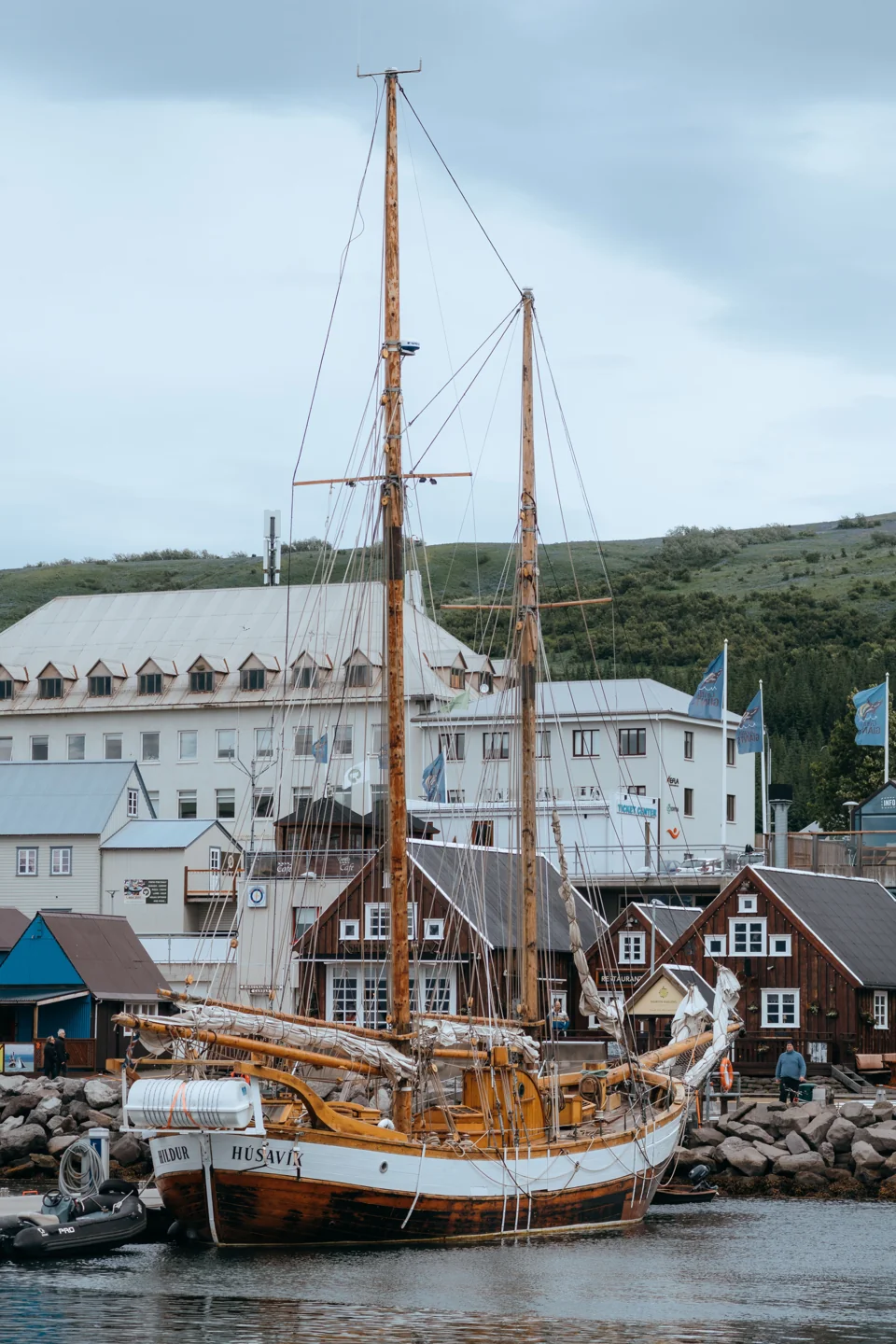 A wooden sailing vessel moored beside Húsavík’s waterfront buildings