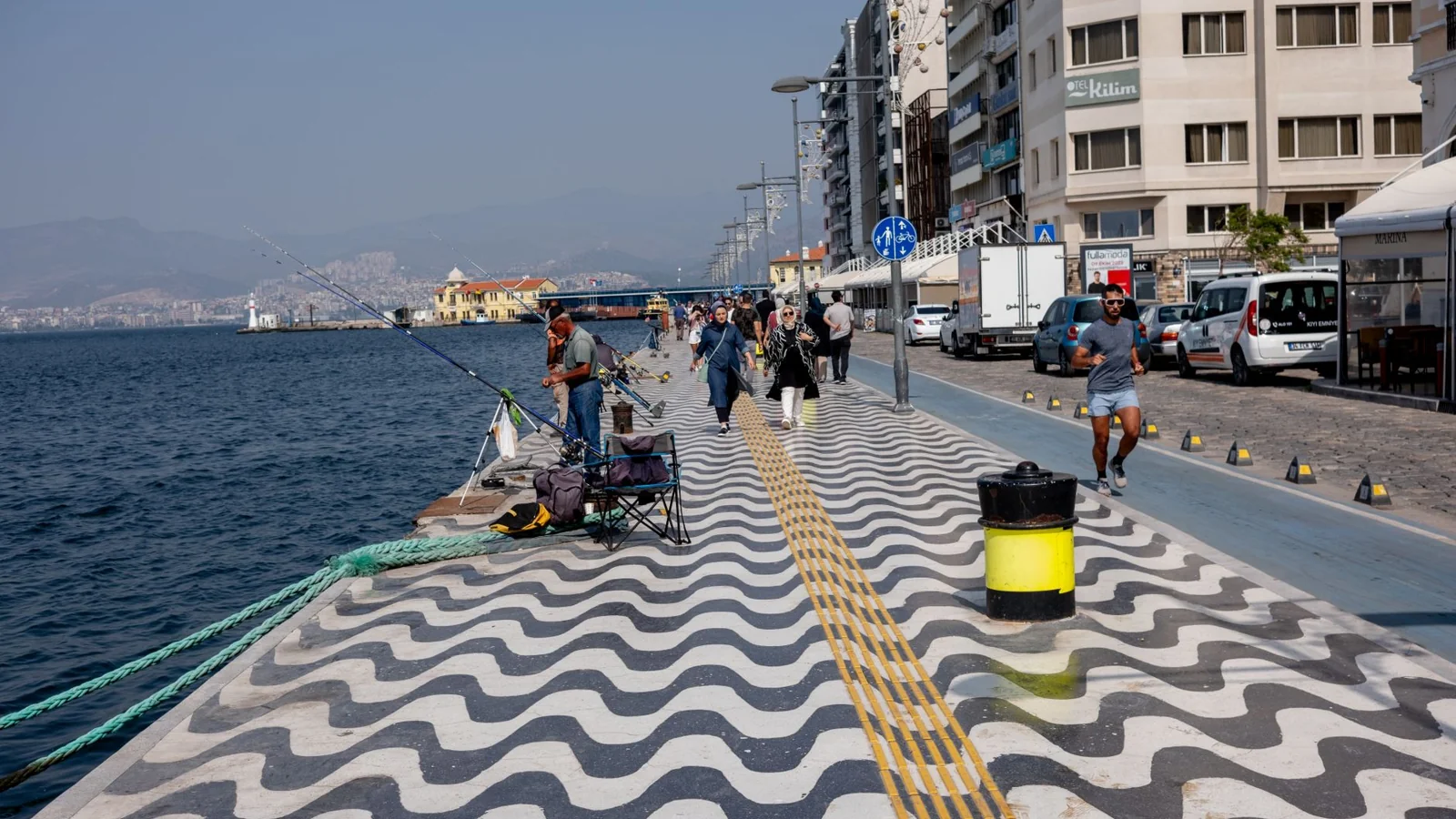 Walkers and anglers beside İzmir’s gulf on the wave-patterned waterfront pavement.