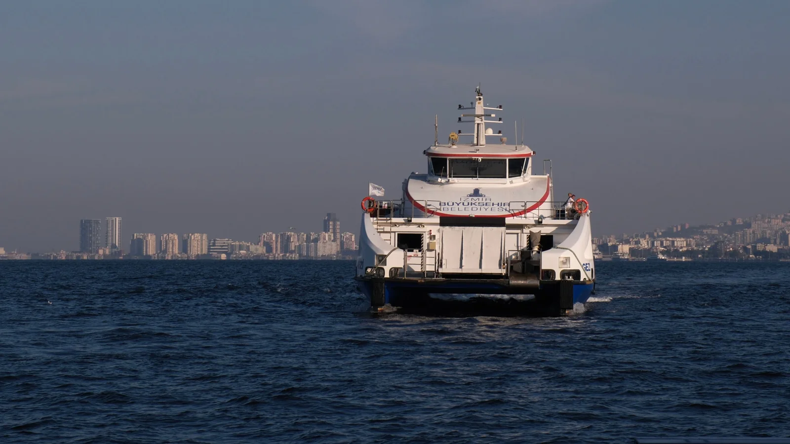 A passenger ferry approaches İzmir’s waterfront with the city skyline behind it.