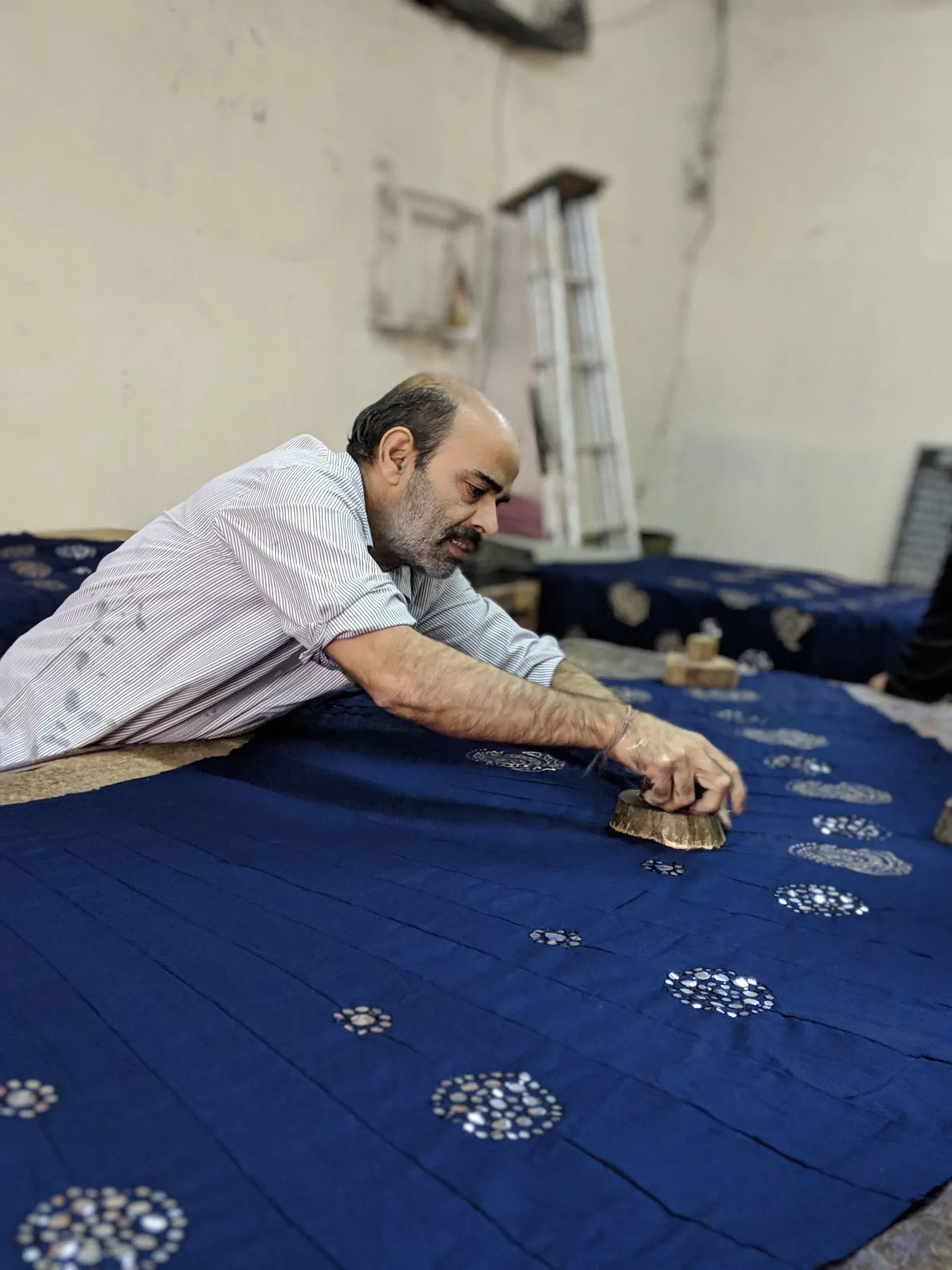 A Jaipur craftsperson hand-printing a patterned blue textile with a wooden block