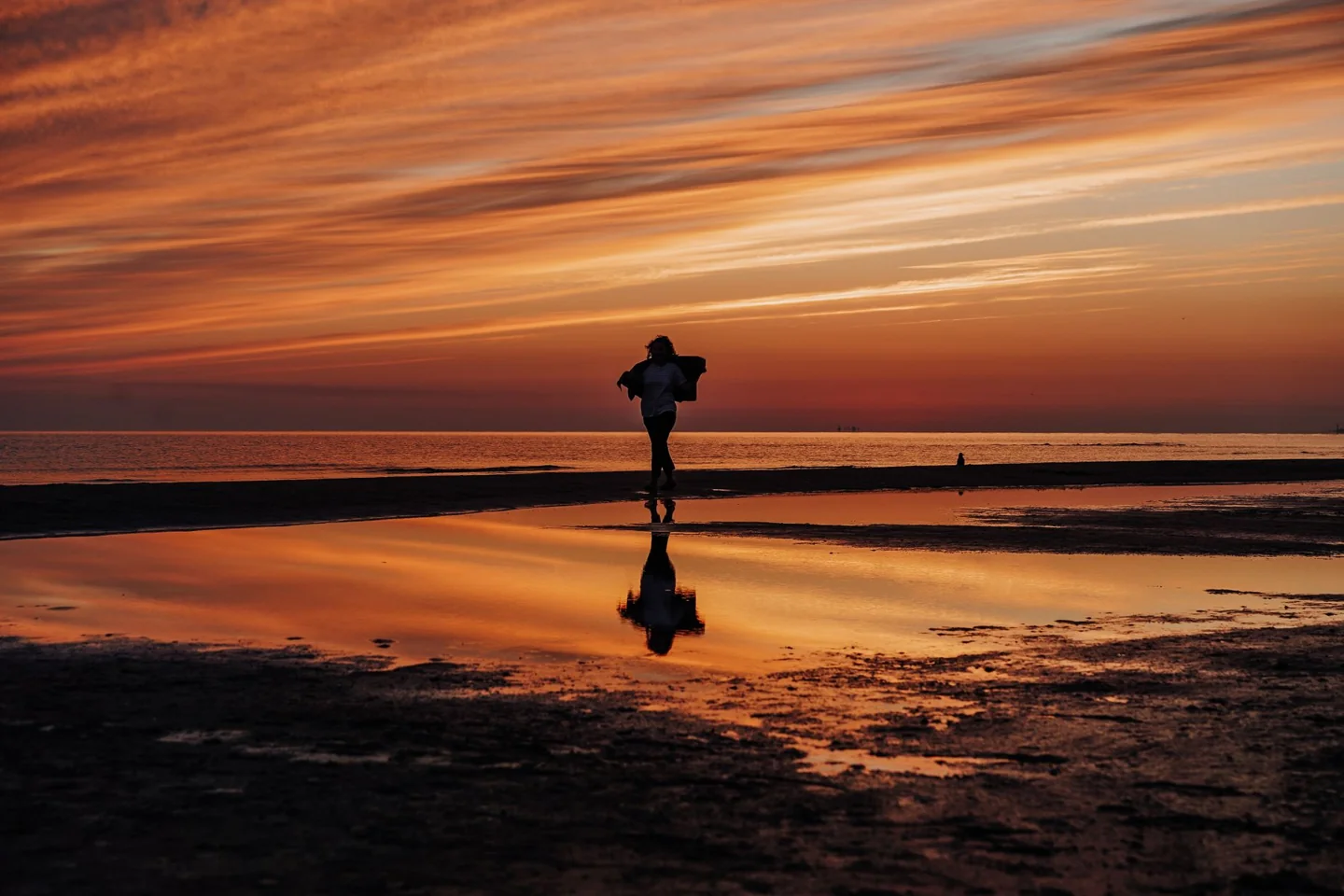 A person silhouetted against orange light reflected on Jūrmala’s wet shoreline