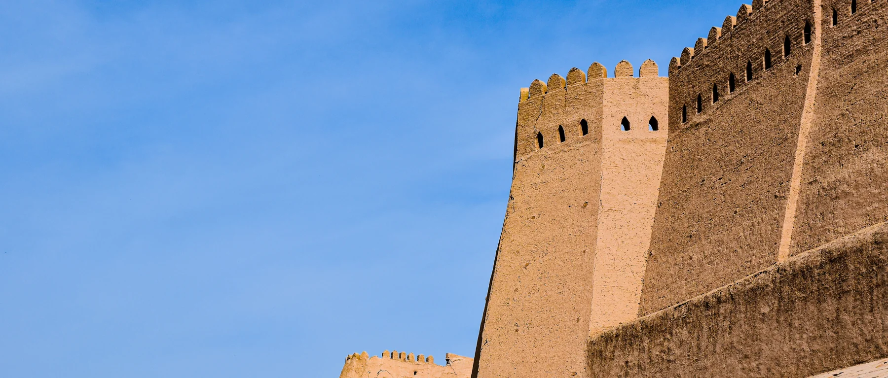 Earthen bastions and crenellated walls of Itchan Kala in Khiva against a blue sky
