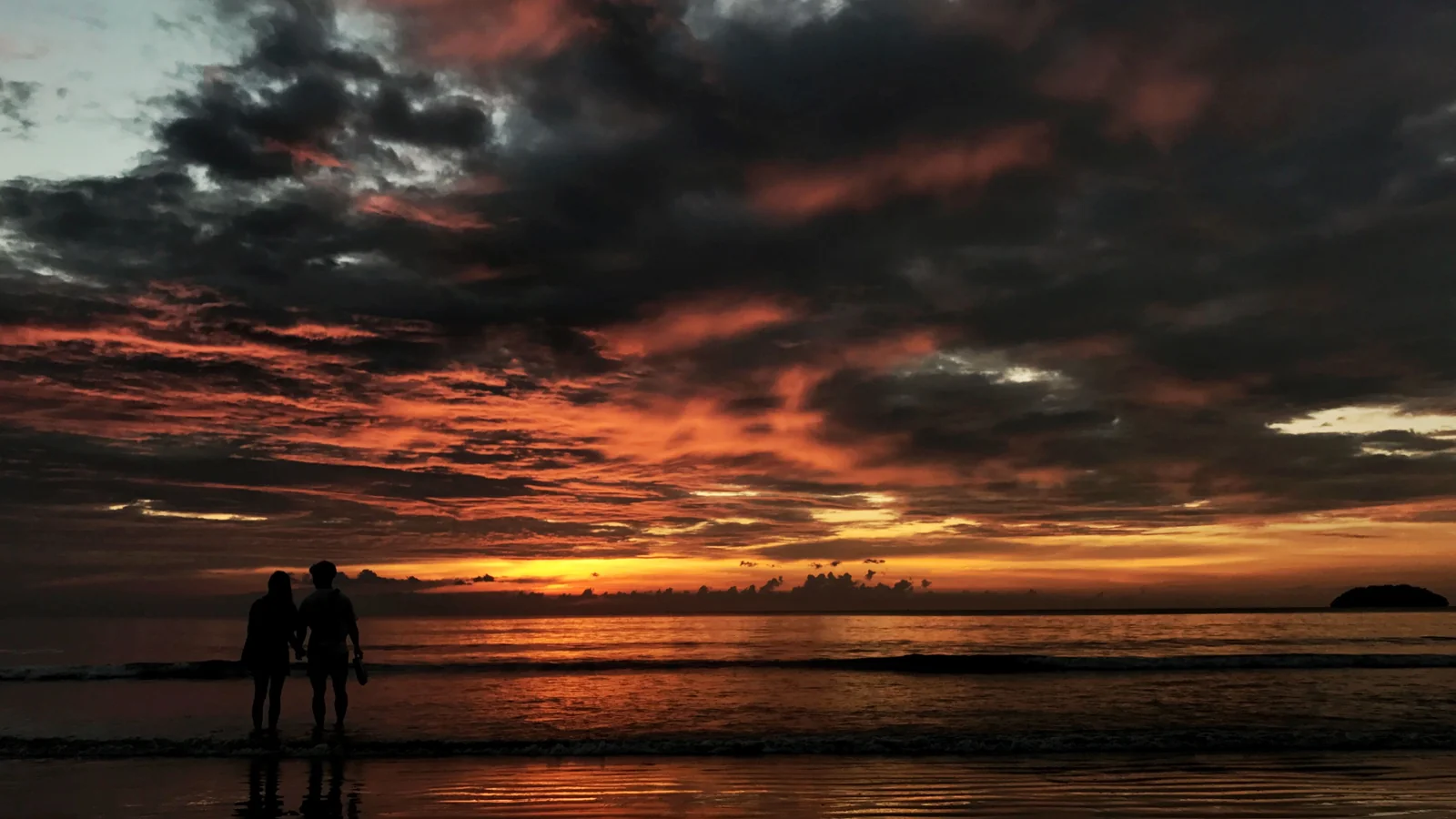 People silhouetted on a Kota Kinabalu beach beneath a dramatic sunset sky.