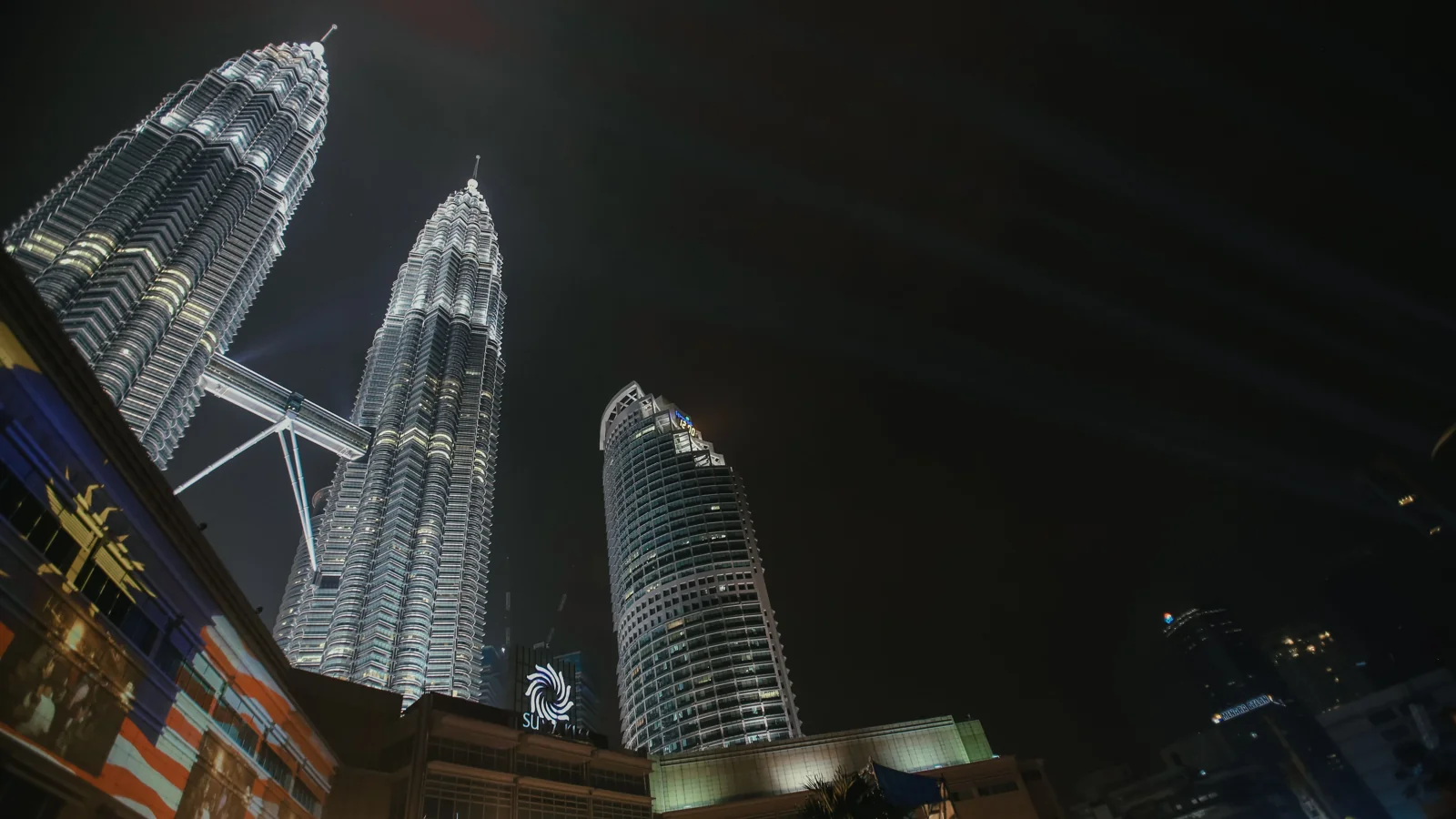 The illuminated Petronas Twin Towers rising above the neighbouring buildings at night.