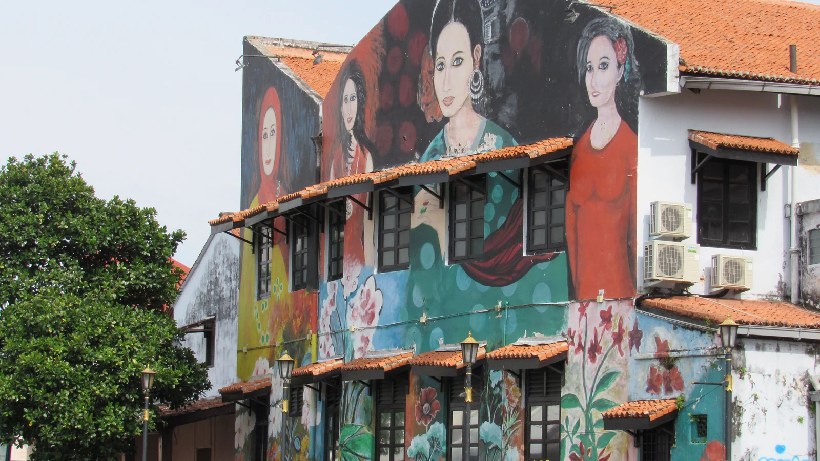 Colourful cultural murals covering a riverside shophouse facade in Malacca.