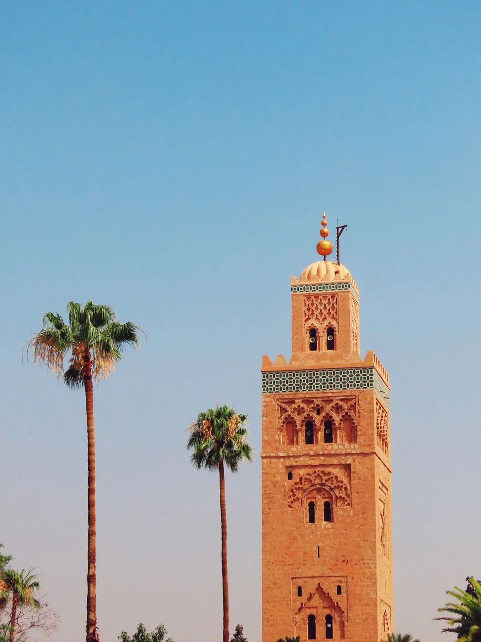 Iconic Koutoubia Mosque tower with palm trees in Marrakech against a clear blue sky.