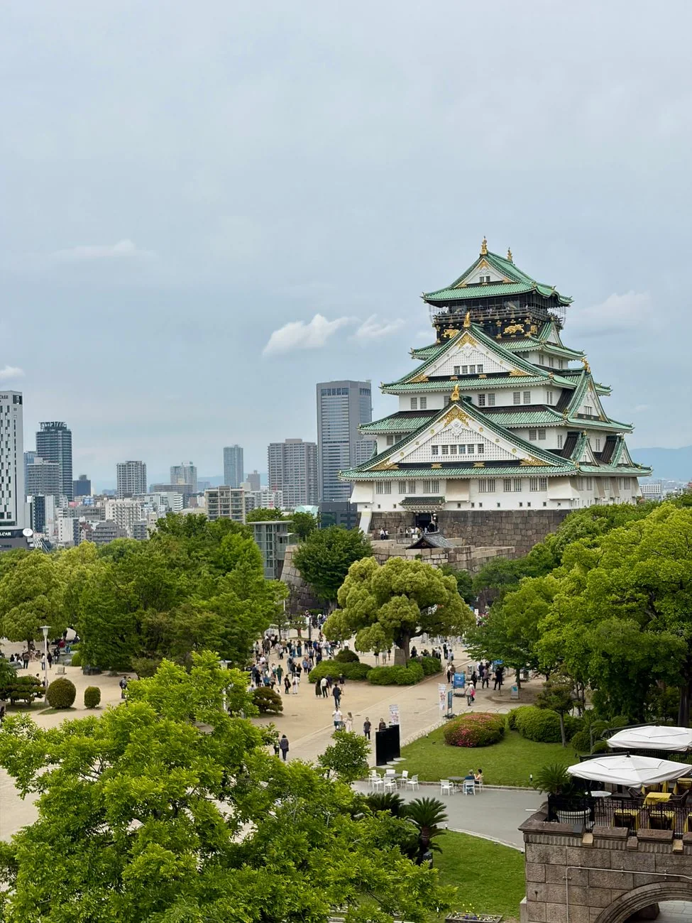 Osaka Castle’s green-roofed tower beyond the park trees and paths