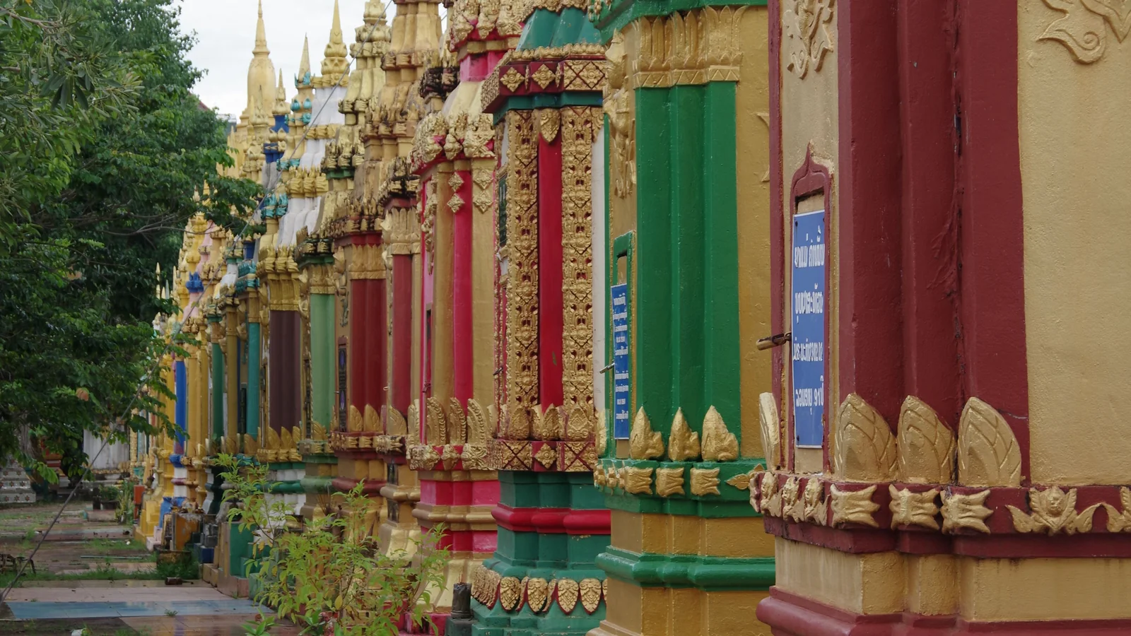A row of gold, red and green funerary stupas beside the path at Wat Phabad in Pakse.