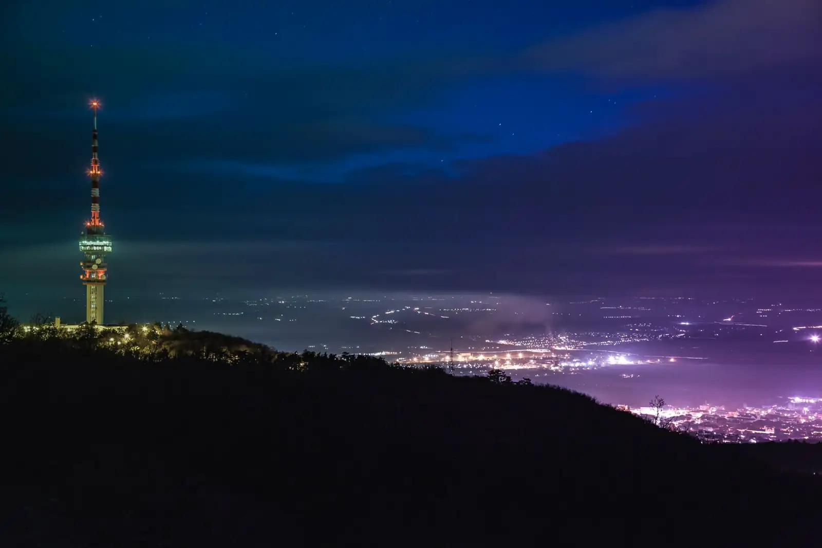 Pécs TV Tower illuminated on Misina above the city lights at night