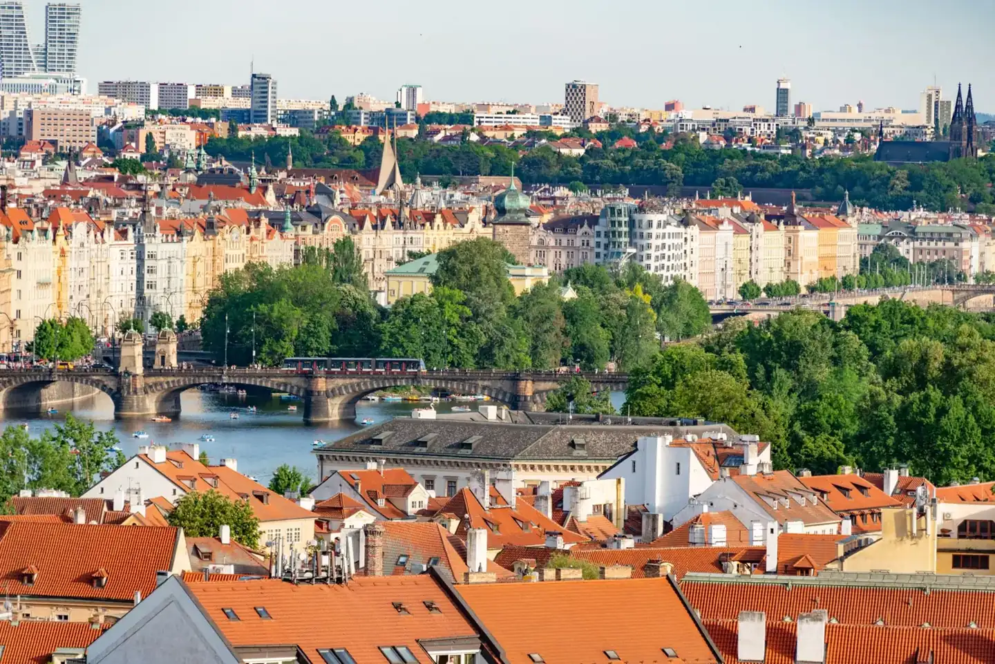 A tram crossing the Vltava below Prague’s Old Town skyline, viewed over red Lesser Town rooftops