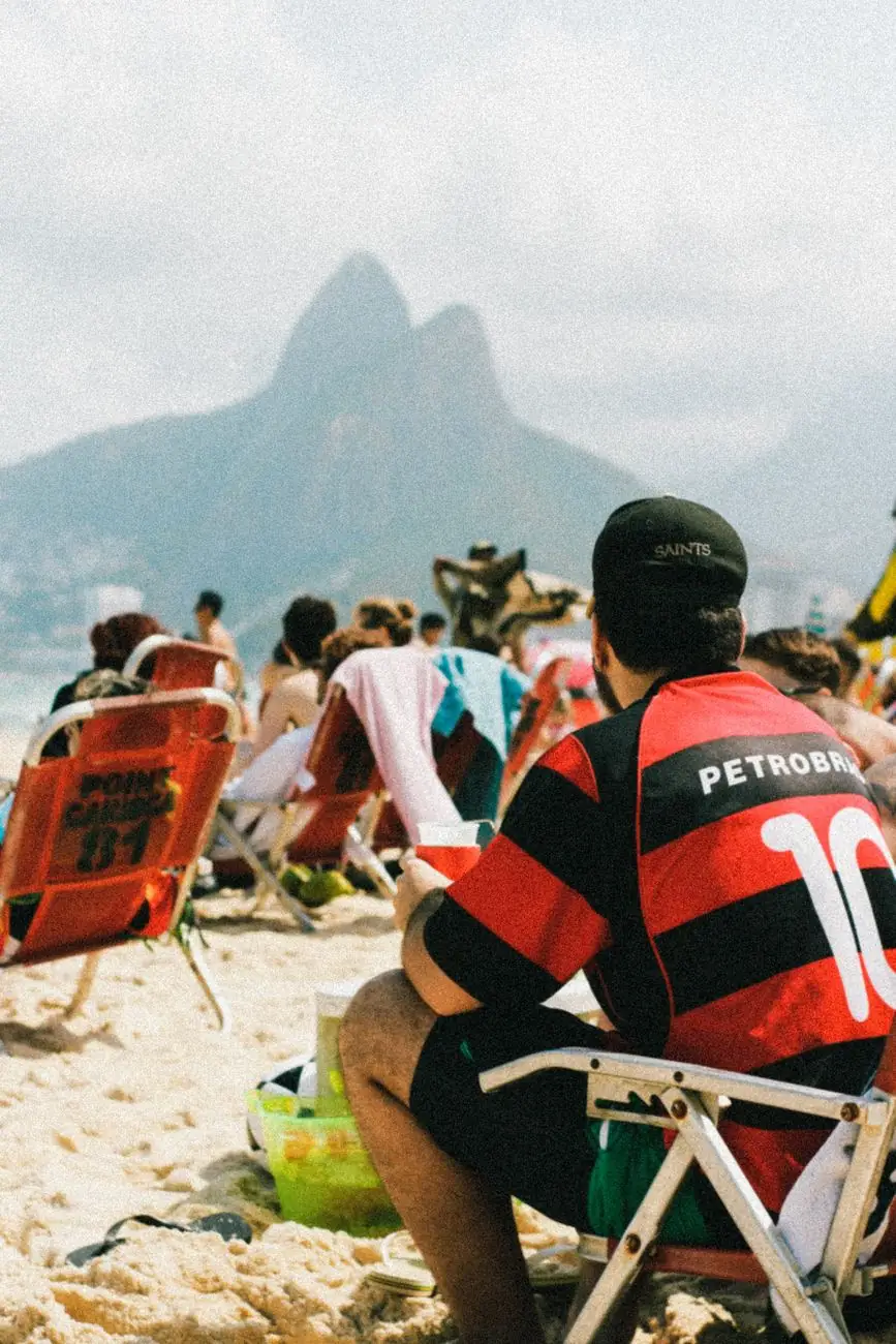 People sitting on Ipanema beach with Rio’s Dois Irmãos peaks in the distance