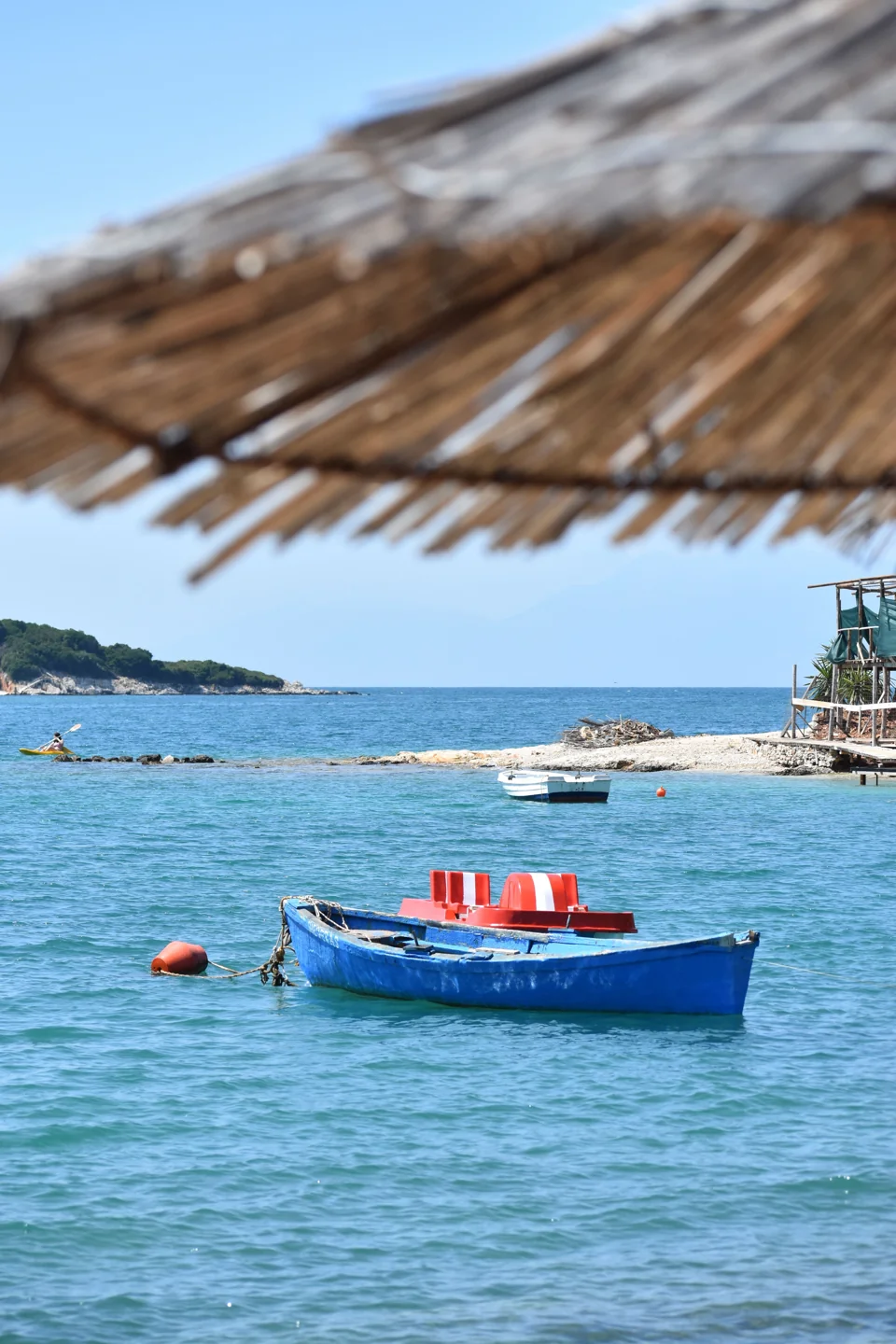 Small boats on clear water beside the shore and wooded islands of Ksamil