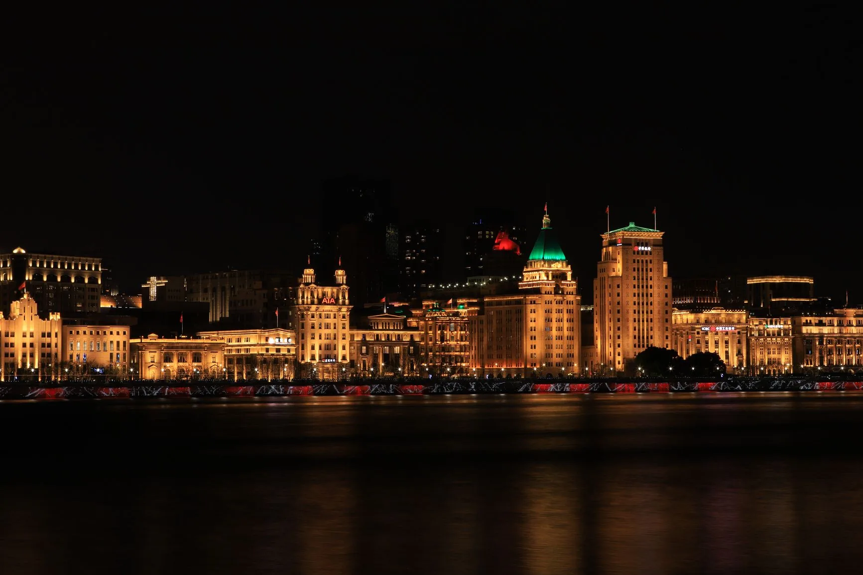 Illuminated historic buildings on Shanghai’s Bund, including the green-roofed Peace Hotel
