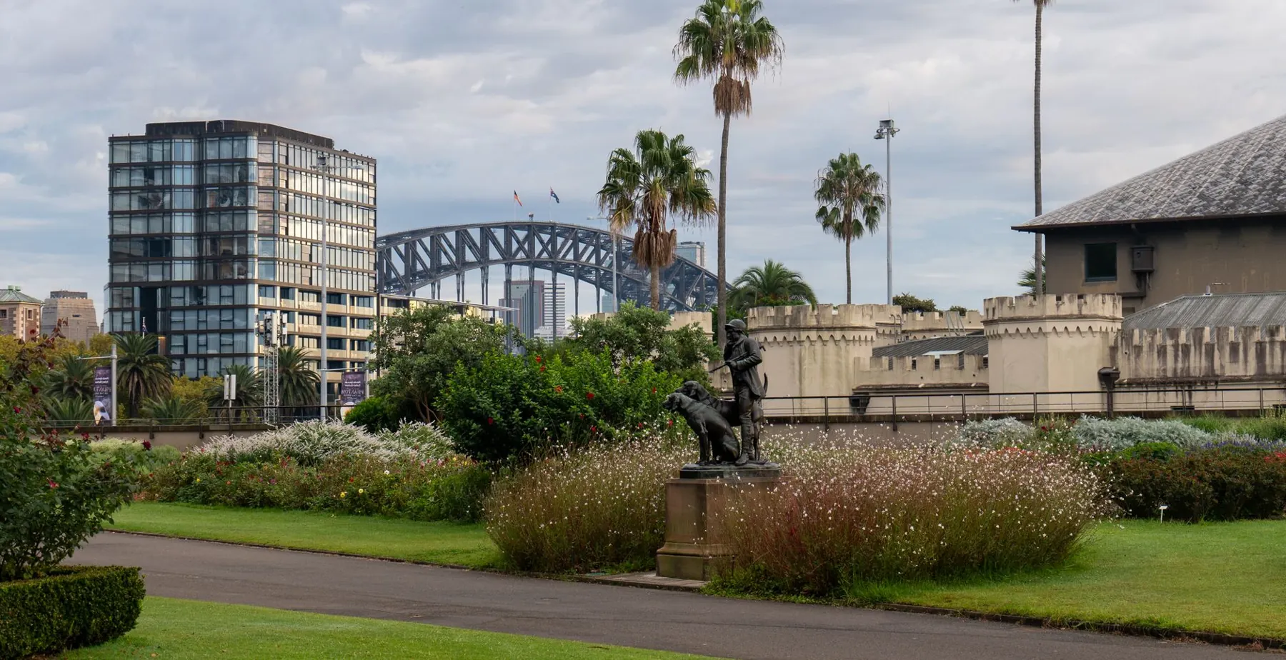 Garden beds and the Huntsman and Dogs sculpture beside Sydney Conservatorium, with Harbour Bridge beyond