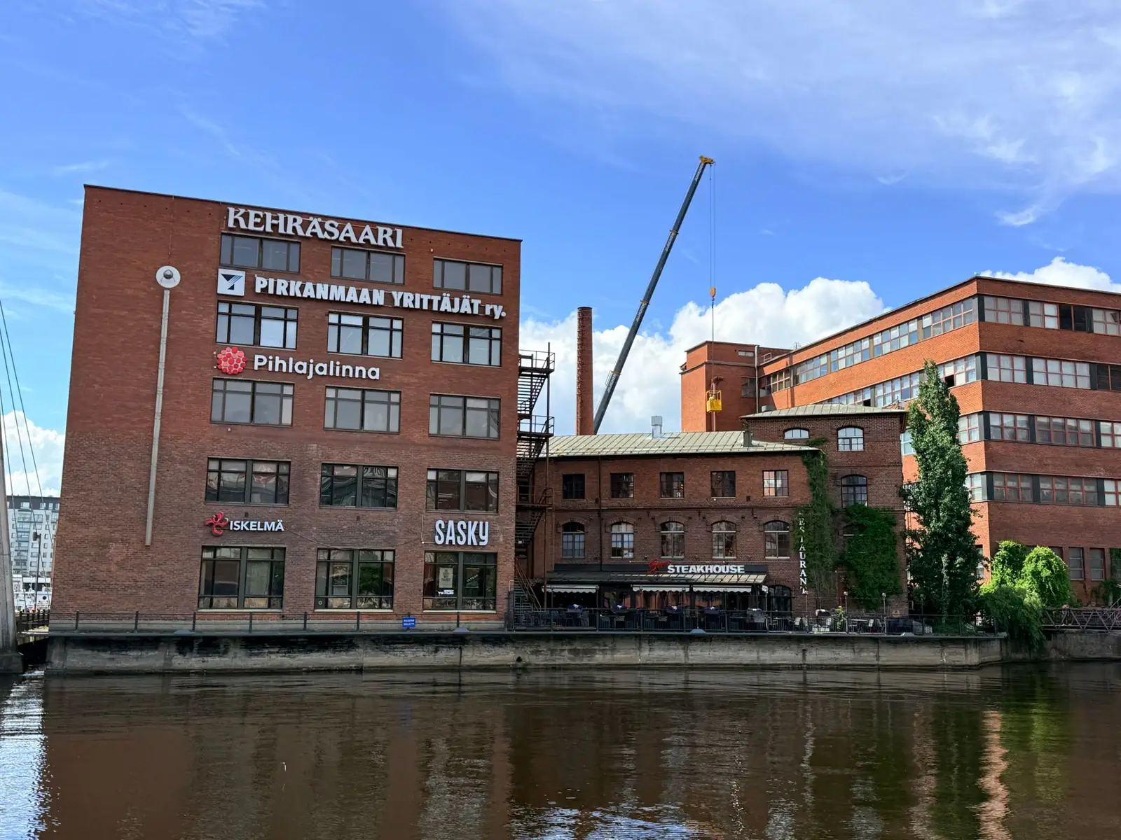 Scenic view of Kehräsaari red brick buildings along the river in Tampere, Finland, on a sunny day.