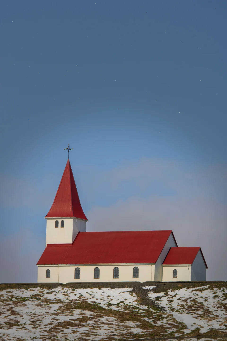Víkurkirkja’s white walls and red roof on a wintry hillside