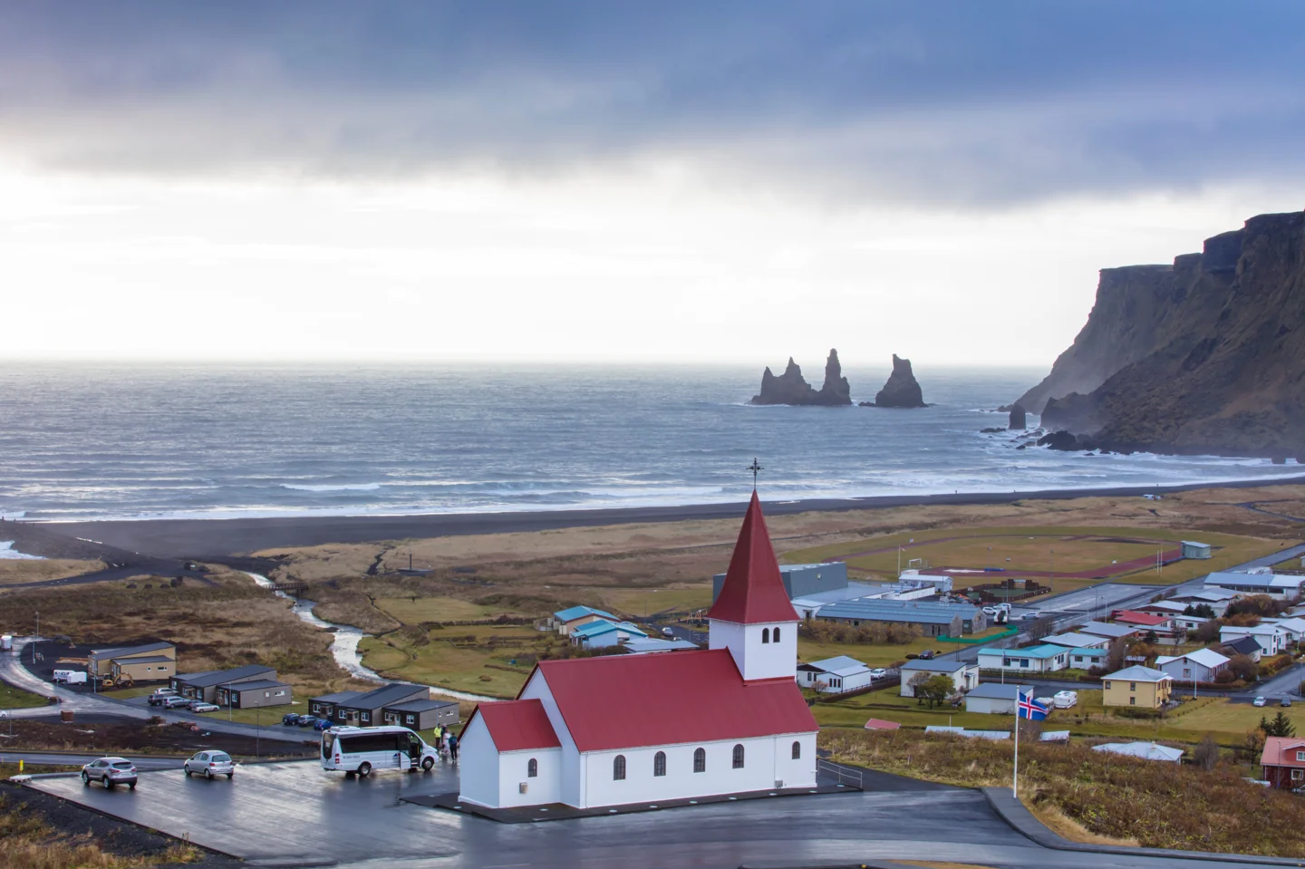 Víkurkirkja above Vík village with the sea and Reynisdrangar in the distance