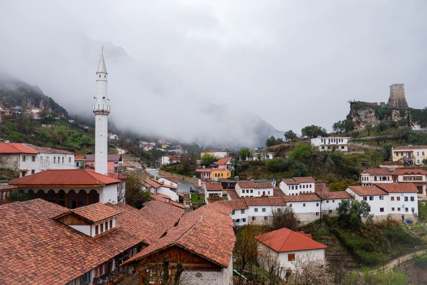 Berat rooftops and a minaret beneath the castle hill in misty light