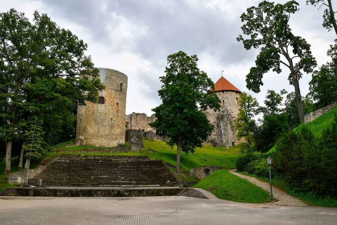 Cēsis Medieval Castle’s stone towers and park paths beneath leafy trees