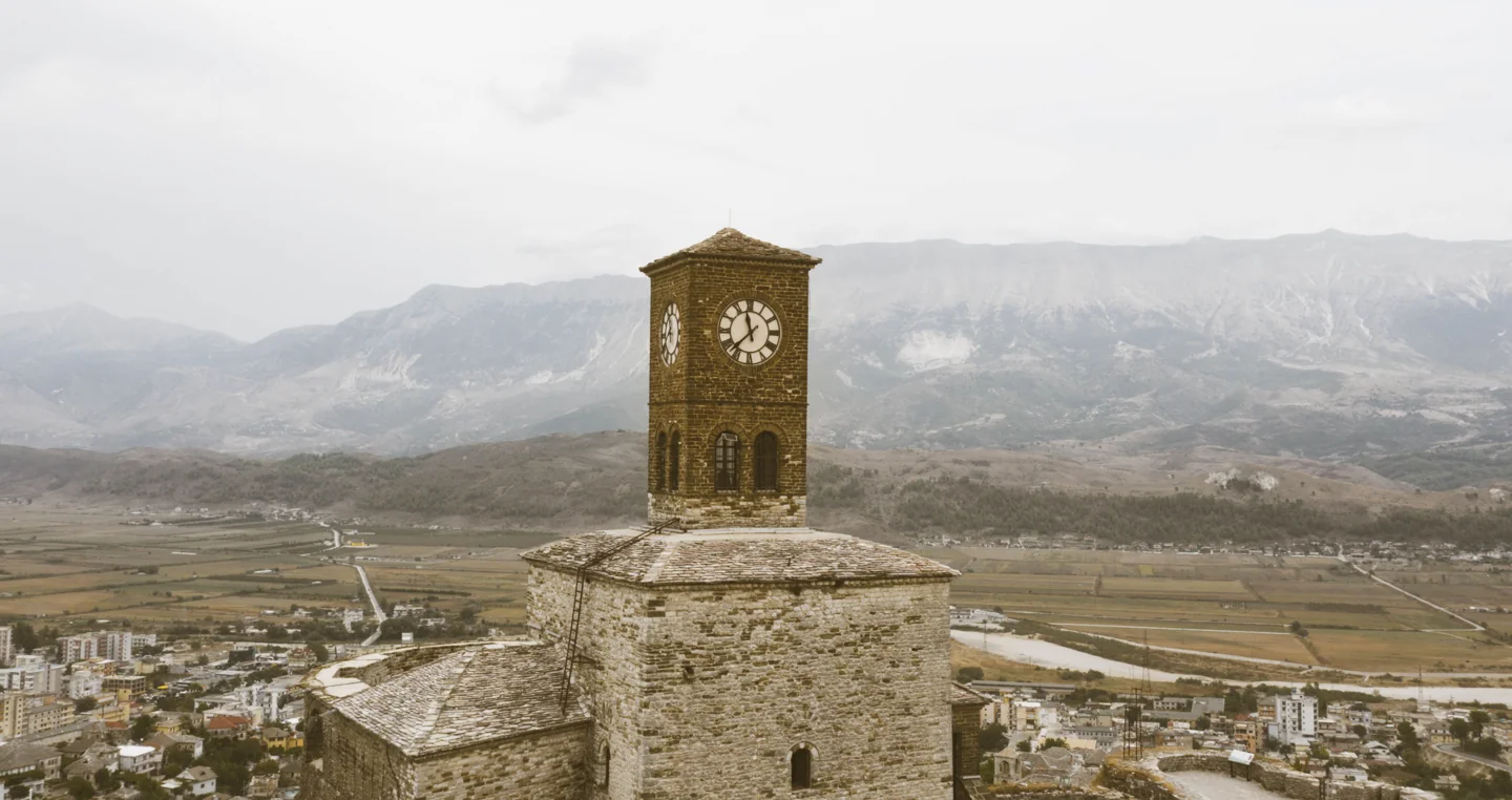 Gjirokastër Castle clock tower above stone walls with the Drinos valley and mountains beyond