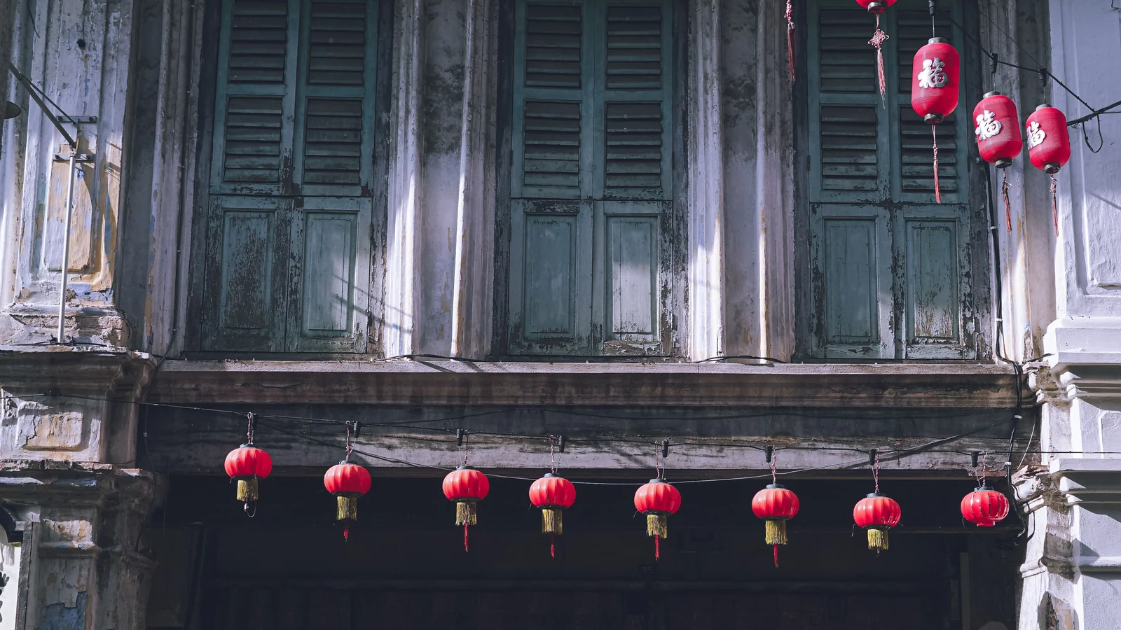 Weathered upper-floor wooden shutters and red lanterns on a heritage shophouse in Ipoh Old Town.