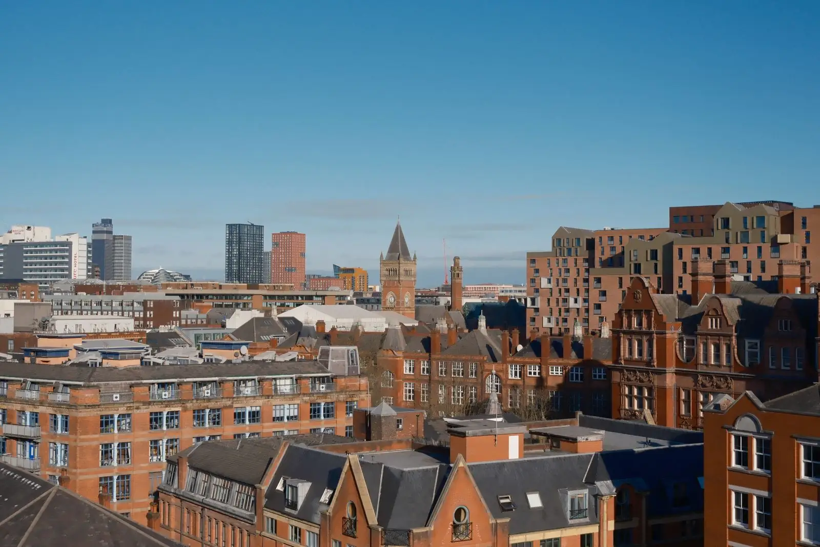 Manchester rooftops and civic architecture beneath a clear blue sky