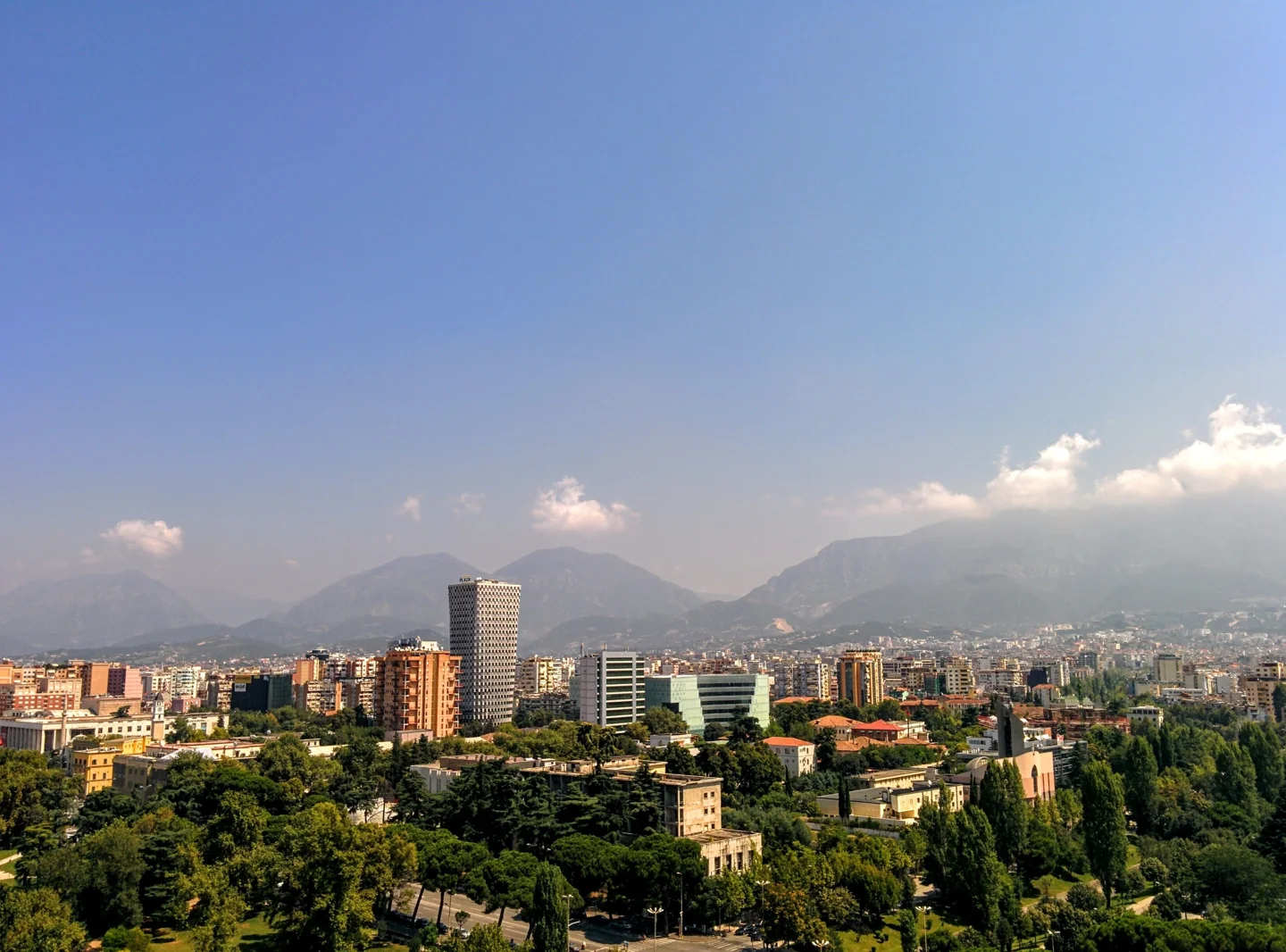 Tirana city skyline with tree-lined central streets, twin office towers and mountains in the distance